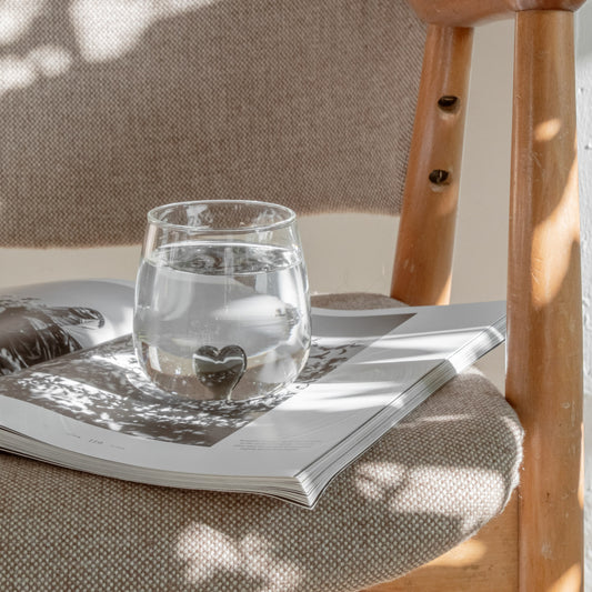 Figurglas Herz schwarz mit Herzform am Boden, gefüllt mit Wasser, auf offenem Buch auf einem gepolsterten Stuhl
