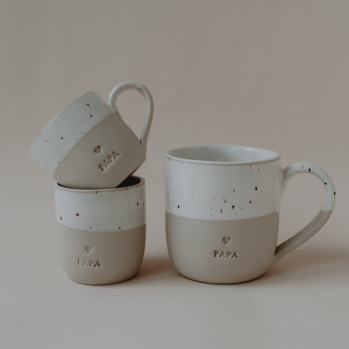 Drei Cappuccinotassen in verschiedenen Größen, zwei stehen, eine ist seitlich aufgesetzt, alle mit PAPA-Prägung.