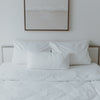 Gemachtes Bett mit 3 Kissen und einer umgeklappten Ecke der Decke und kleinen schwarzen gedruckten Herzen.