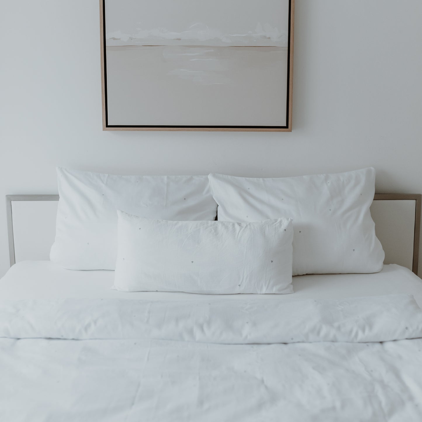 Gemachtes Bett mit 3 Kissen und einer umgeklappten Ecke der Decke und kleinen schwarzen gedruckten Herzen.