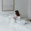 Eine junge Frau sitzt im Bett und guckt sich die Bettdecke an und die kleinen Herzen darauf. Hinter ihr sind noch 3 Kissen und über dem Bett hängt ein Bild.
