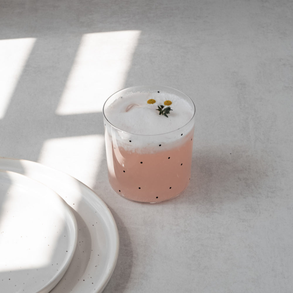 Punktglas mit rosa Drink und Blüten, modernes Trinkglas mit schwarzem Punktemuster für stilvolle Tischdeko
