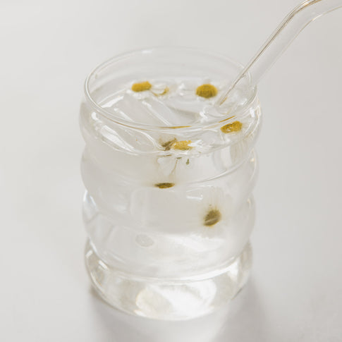 Glas mit Eis und Blüten im Wasser, minimalistisch inszeniert