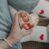 Hand hält eine Herzschale mit Vanilleeis und Erdbeeren, gemütlicher Snackmoment.