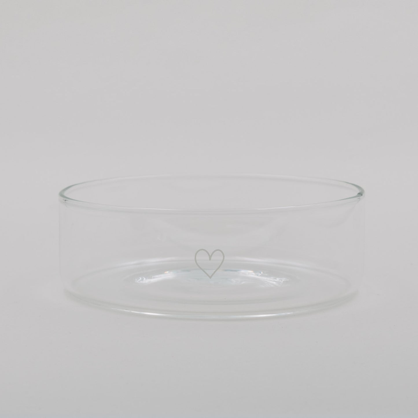 Transparente Glas-Schale mit zartem Herzmotiv, schlicht und minimalistisch vor hellem Hintergrund.