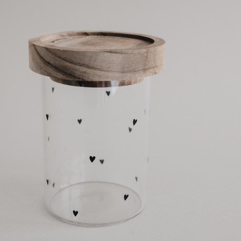 Kleines Vorratsglas mit schwarzen Herzen und Holzdeckel vor hellem Hintergrund