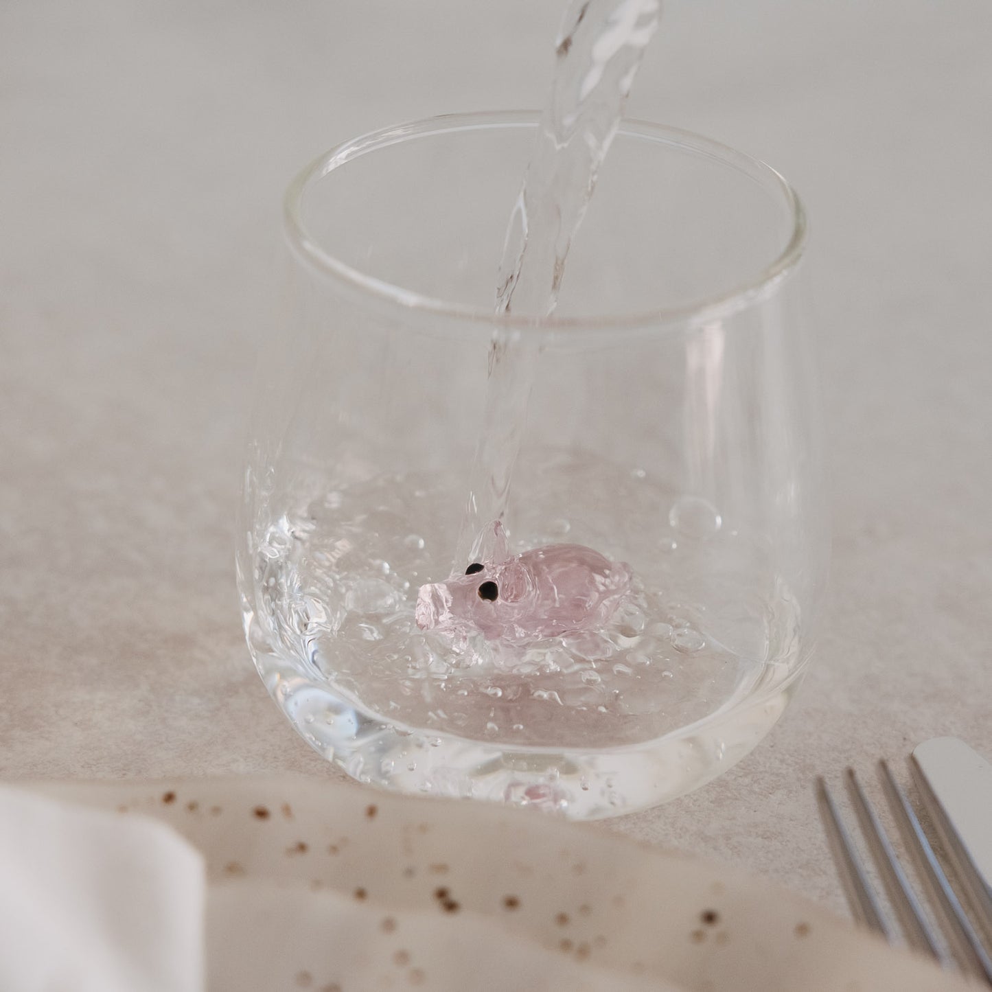 Trinkglas mit rosa Schwein im Boden, Wasser wird eingegossen, modernes Glasdesign