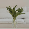 Glasvase mit Blumenwiesen-Motiv und weißen Tulpen auf einem Tisch in heller Wohnumgebung