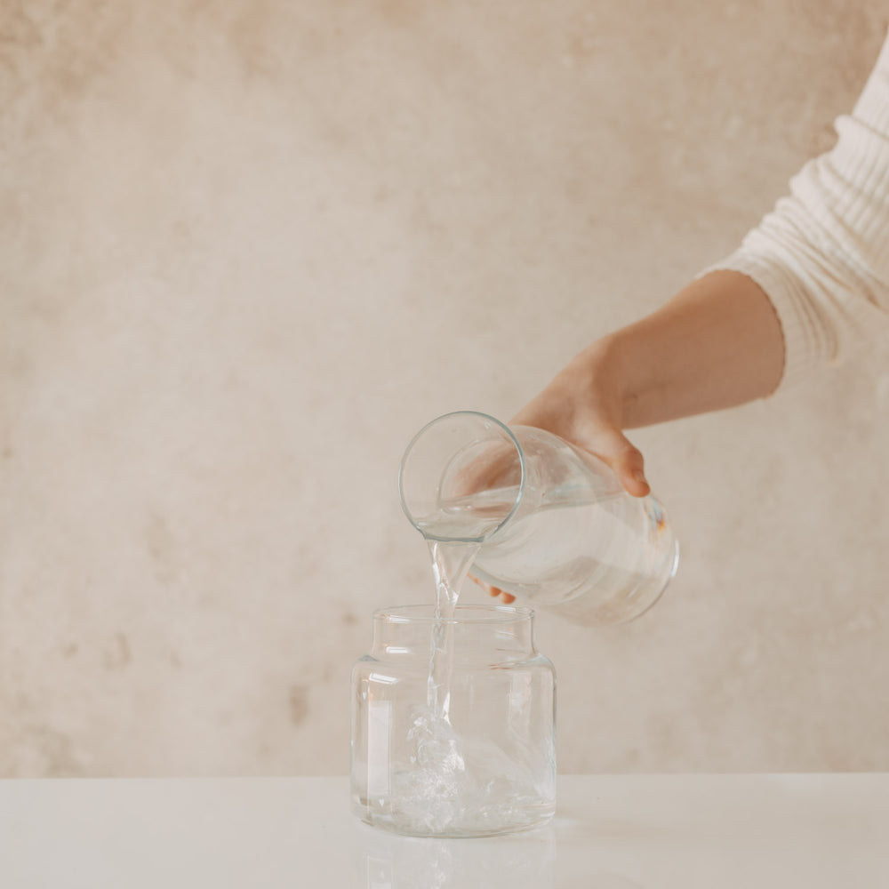 Hand gießt Wasser aus Glas Karaffe in Vase mit Herzmotiv