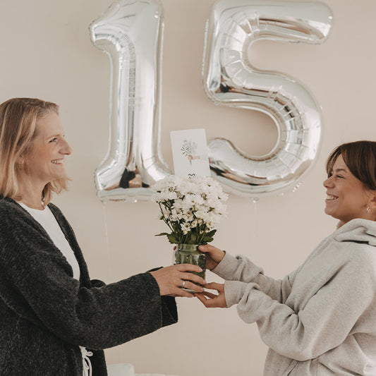 Zwei lachende Frauen mit Blumenvase vor silbernen Luftballons zum 15. Geburtstag