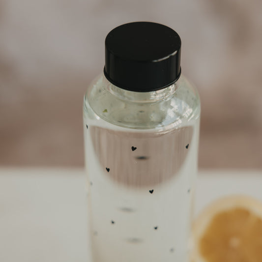 Nahaufnahme Trinkflasche aus Glas mit schwarzen Herzdetails und Schraubdeckel