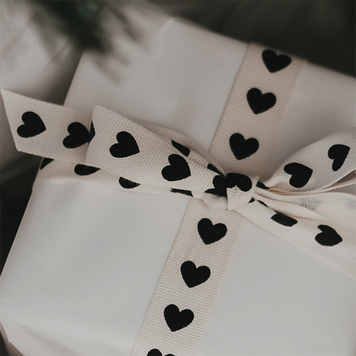 Animiertes Gif mit 3 Bildern: Geschenk mit Baumwollband und schwarzen Herzen verpackt liegt unter einem Weihanchtsbaum