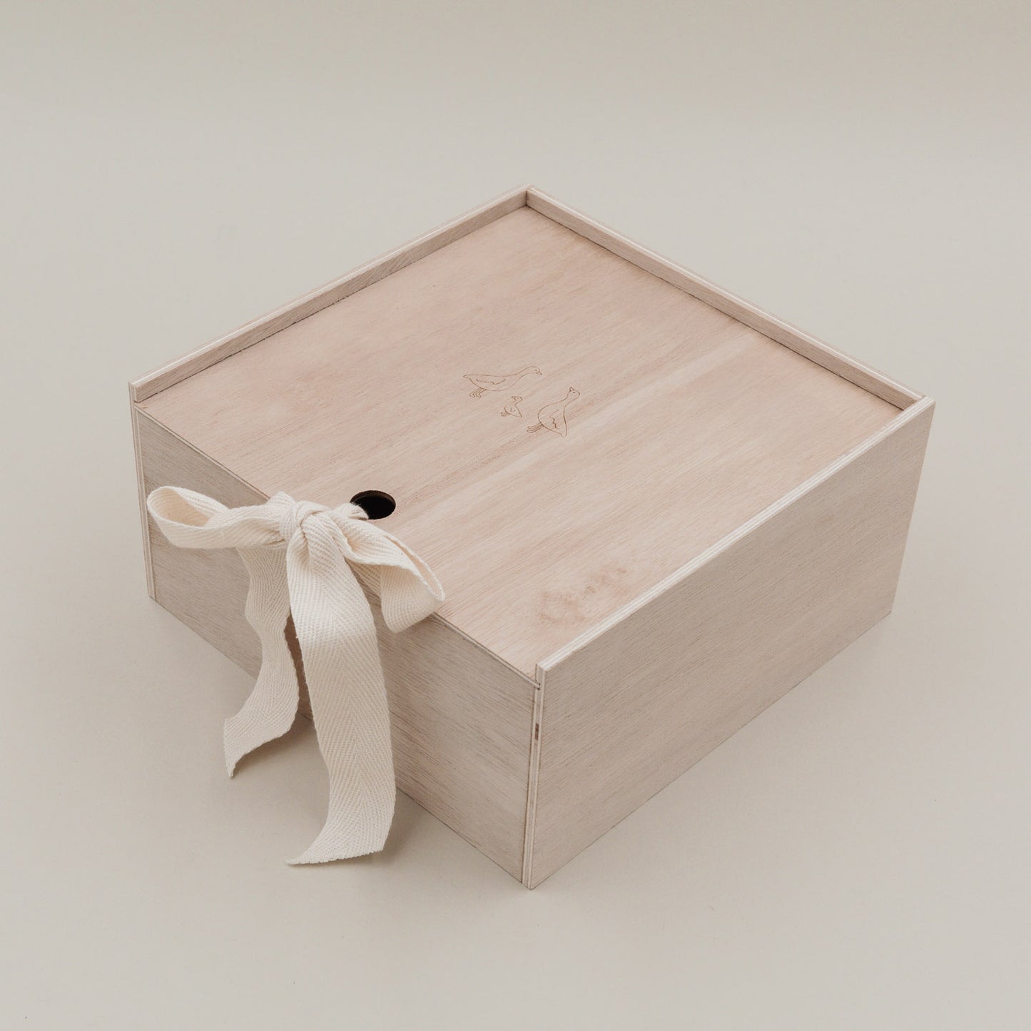 Erinnerungsbox aus hellem Holz mit Gänsegravur und Stoffschleife, frontal fotografiert.