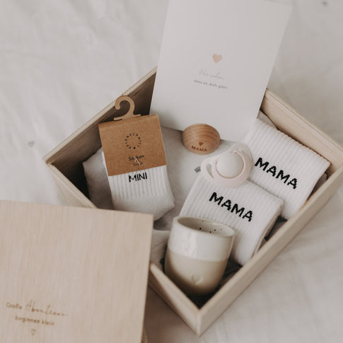 Holz-Erinnerungsbox offen, gefüllt mit Mama- und Mini-Socken, Postkarte, Schnuller und Babybecher.