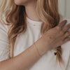 Armband Jackie Gold mit drei Sternen am Handgelenk, kombiniert mit schlichtem T-Shirt und goldenem Ring.
