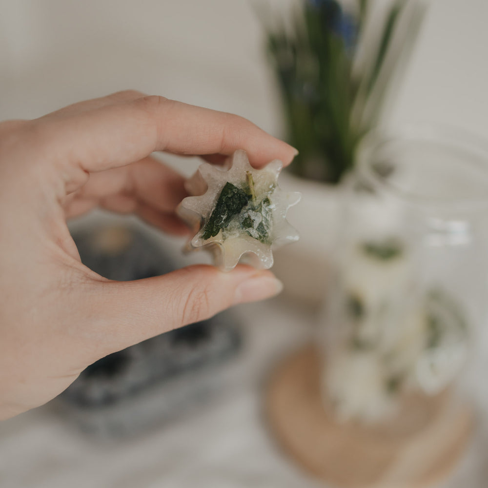 Fertiger Eiswürfel mit Minze aus der grauen Blütenform aus flexiblem Silikon gehalten in einer Hand.