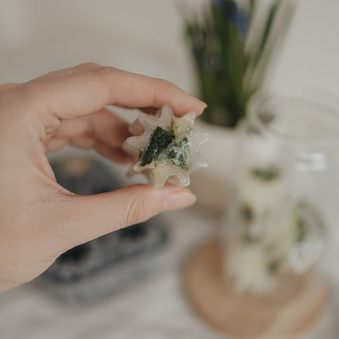Fertiger Eiswürfel mit Minze aus der grauen Blütenform aus flexiblem Silikon gehalten in einer Hand.