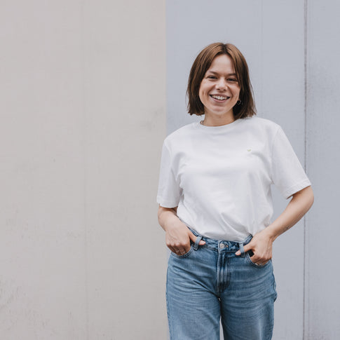 Frau im weißen T-Shirt mit kleinem Herzprint, lässiger Look vor neutralem Hintergrund