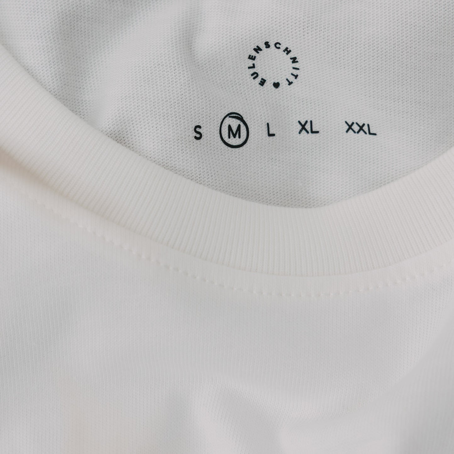 Detail Kragen weißes T-Shirt mit Größenangabe und Eulenschnitt Logo
