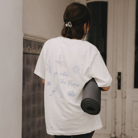 Frau trägt Yogamatte und weißes T-Shirt mit „go with the flow“ Print auf dem Rücken
