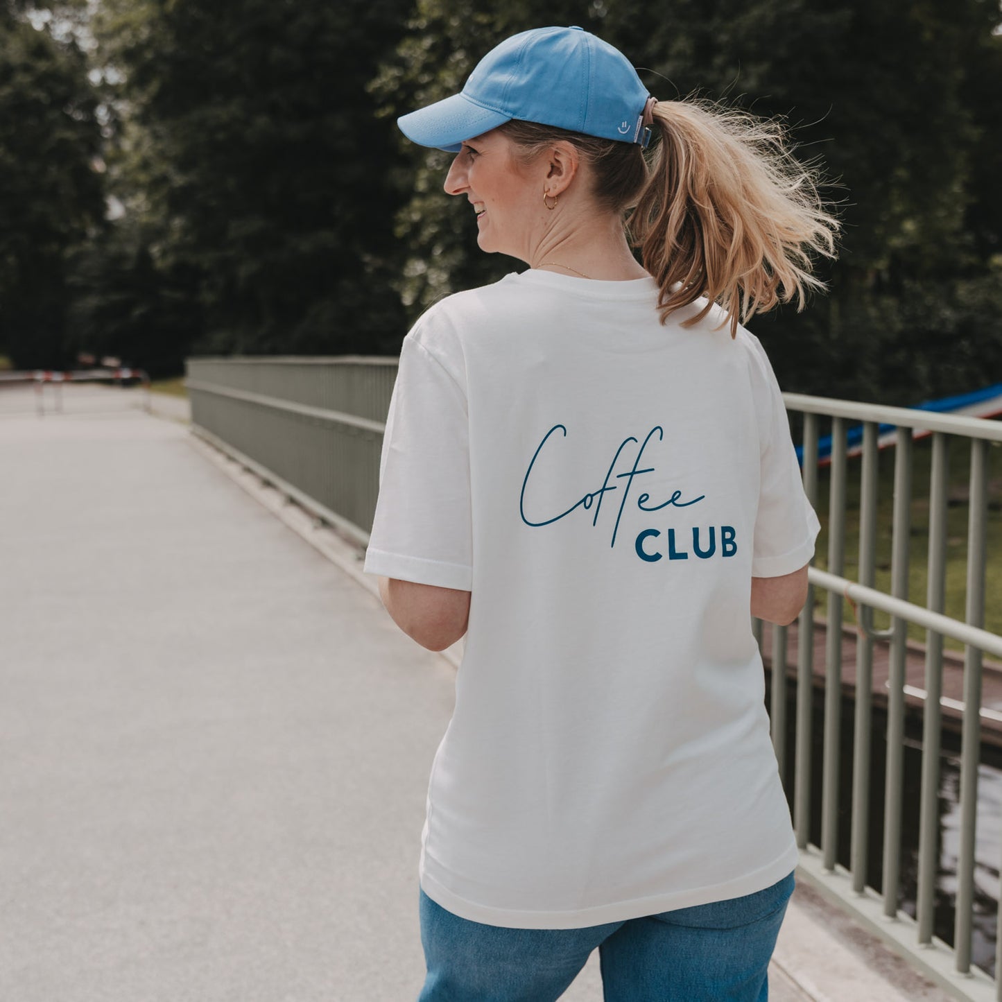 Frau trägt weißes Coffee Club T-Shirt beim Spaziergang, Rückenansicht