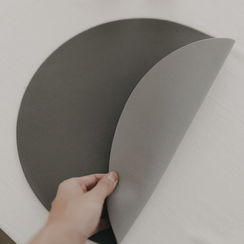 Hand biegt das wendbare graue Platzset, um die dunkle Rückseite zu zeigen.