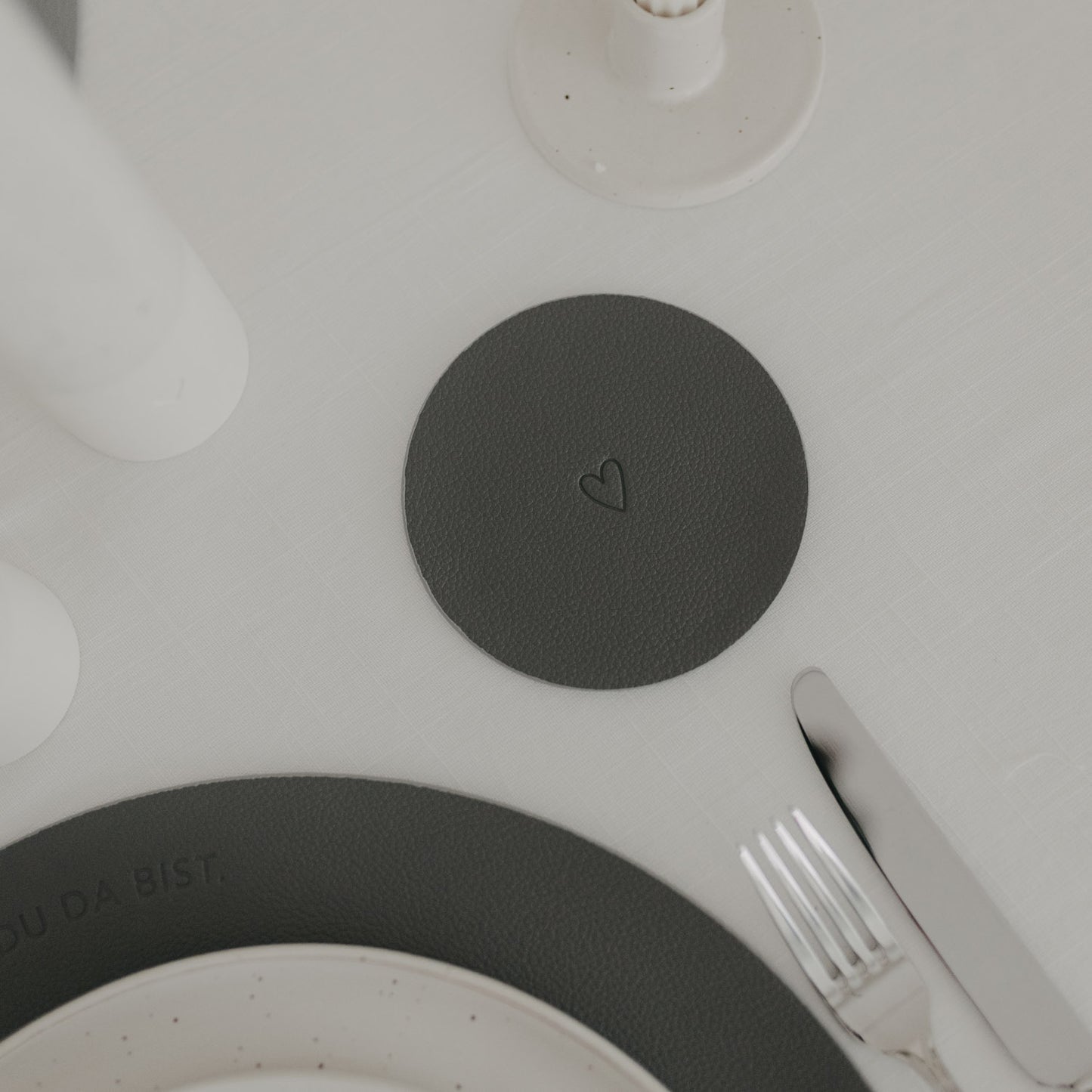 Wendbarer Untersetzer in Dunkelgrau mit eingeprägtem Herzmotiv auf gedecktem Tisch.