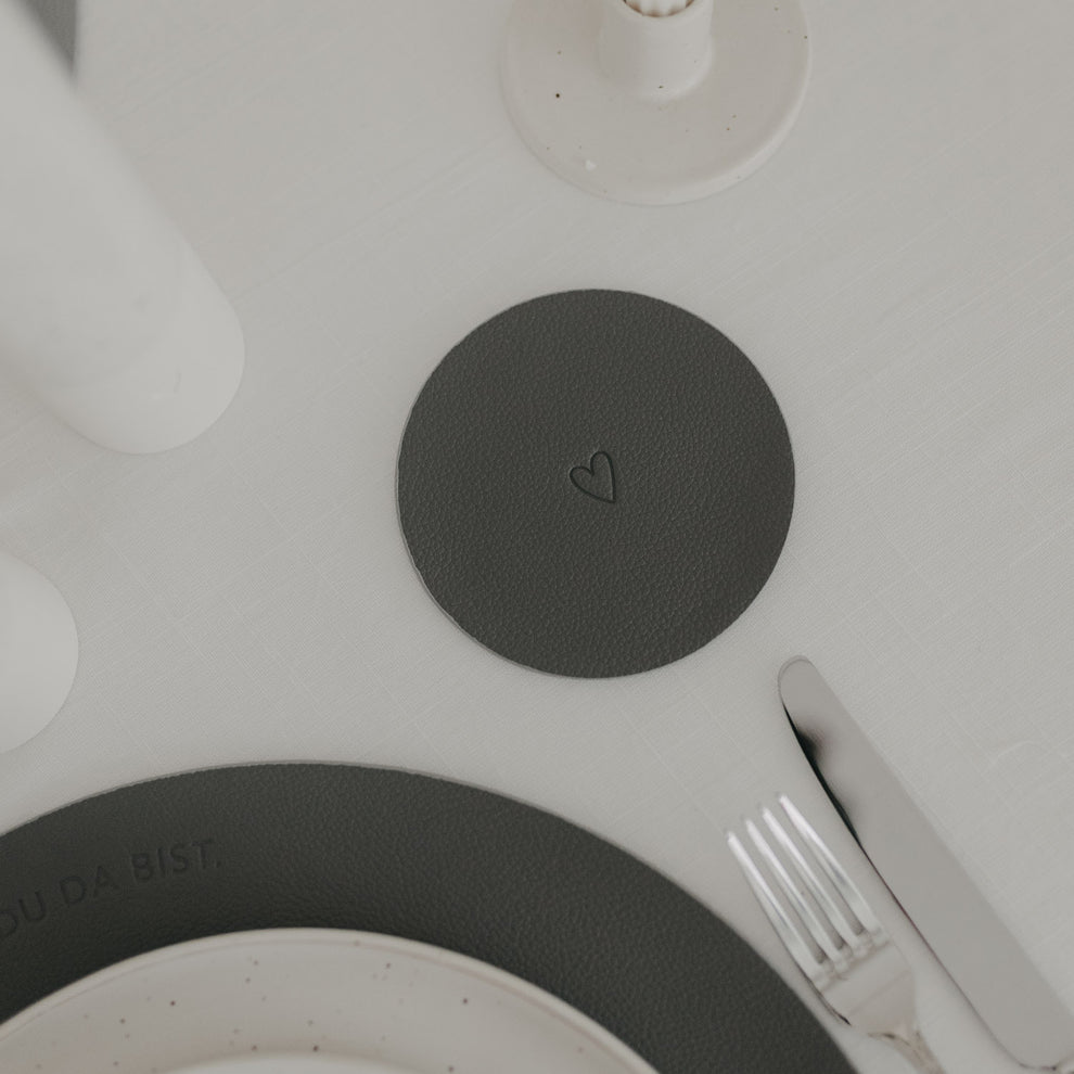Wendbarer Untersetzer in Dunkelgrau mit eingeprägtem Herzmotiv auf gedecktem Tisch.