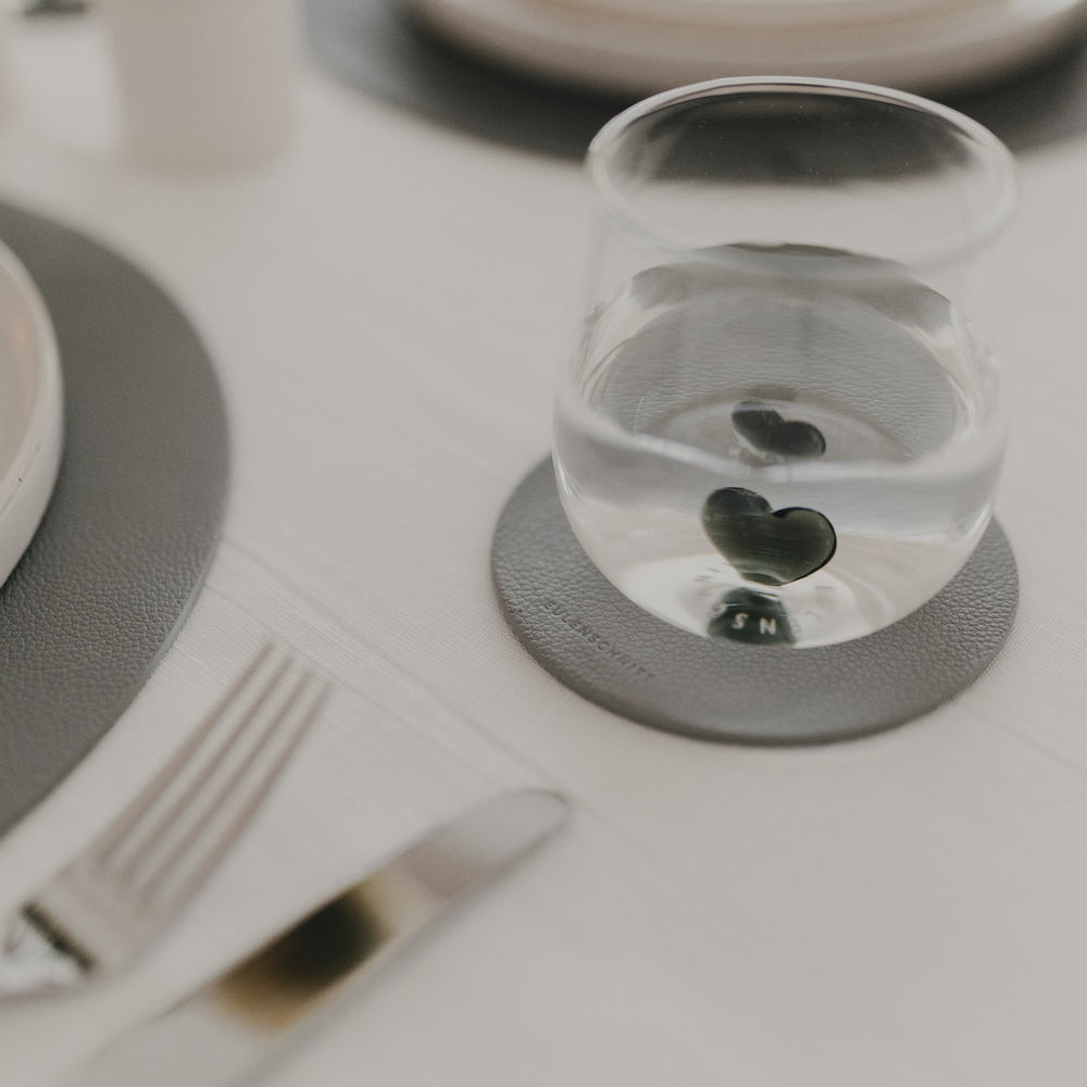 Glas auf grauem Untersetzer mit Eulenschnitt-Logo, passend zu grauem Platzset auf gedecktem Tisch.