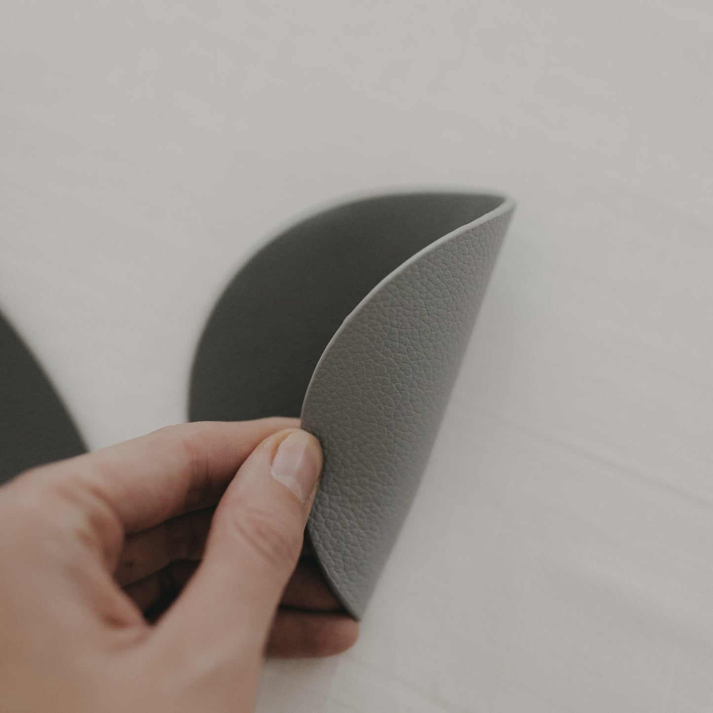 Hand biegt wendbaren Untersetzer in Grau und Dunkelgrau, strukturierte Oberfläche sichtbar.