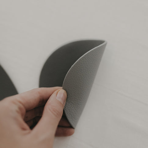 Hand biegt wendbaren Untersetzer in Grau und Dunkelgrau, strukturierte Oberfläche sichtbar.