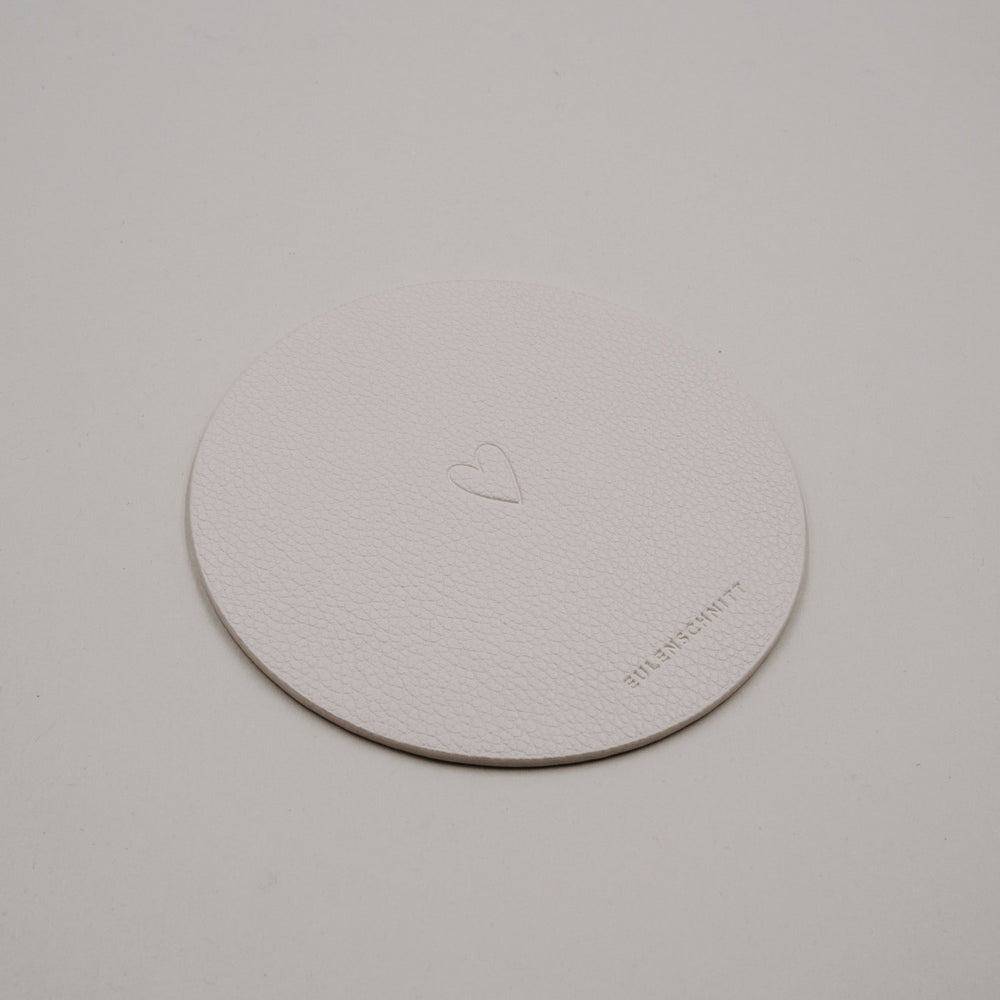 Heller runder Untersetzer aus Kunstleder in Creme mit eingeprägtem Herzmotiv von Eulenschnitt.
