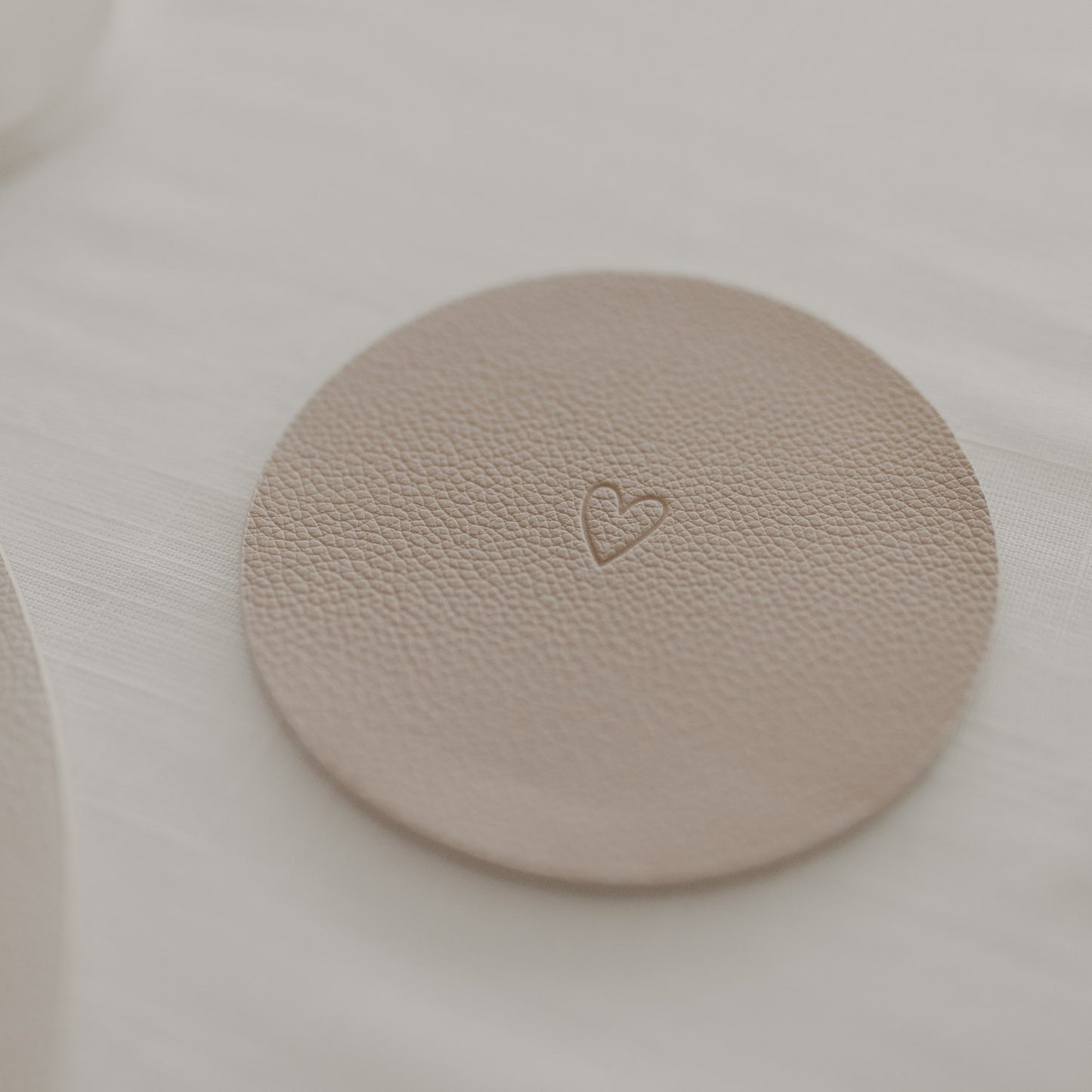 Cremefarbener Kunstleder-Untersetzer mit Herzprägung auf gedecktem Tisch in hellem Ambiente.