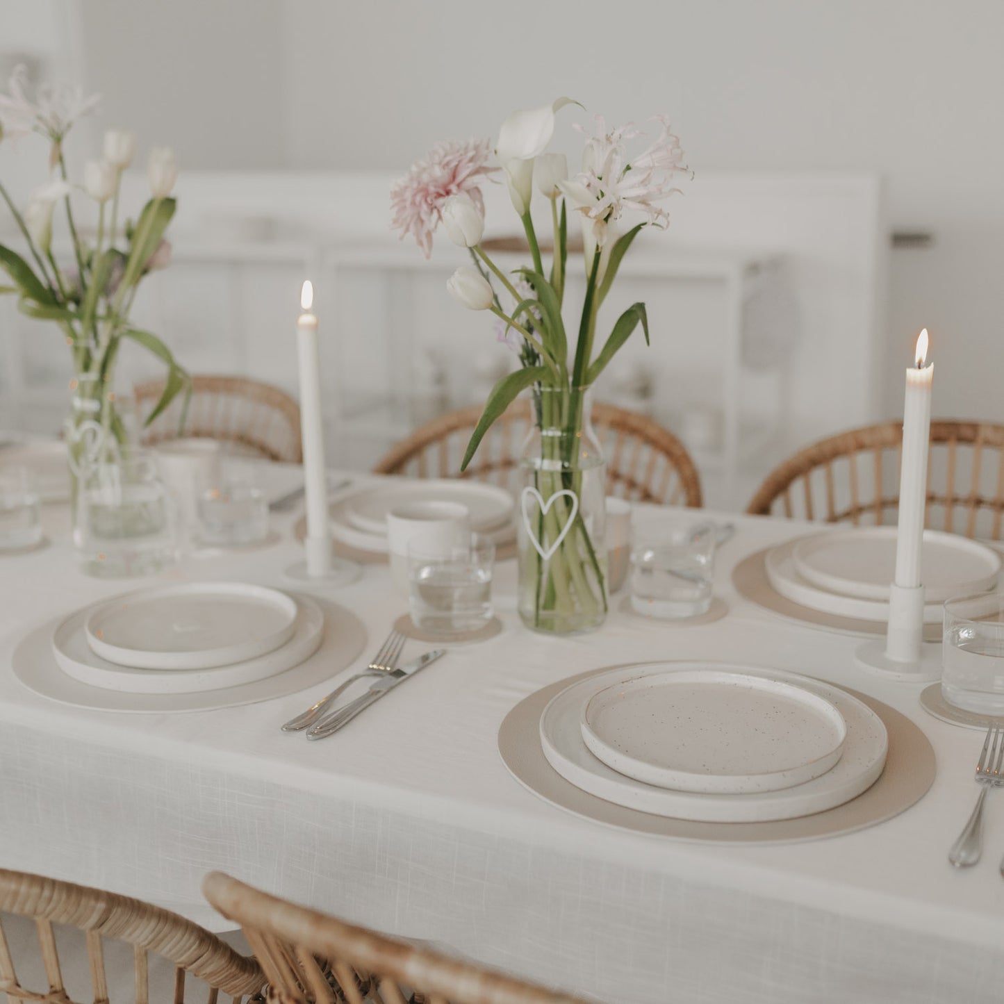 Gedeckter Tisch in Beige mit runden Platzsets aus Kunstleder und Blumenvasen für eine elegante Tischdekoration.
