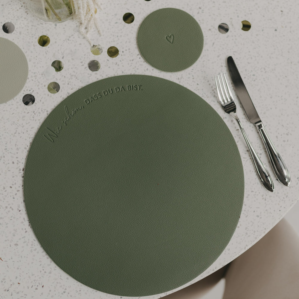 Grünes Platzset mit eingeprägtem Spruch ‚Wie schön, dass du da bist‘ neben Besteck auf gedecktem Tisch