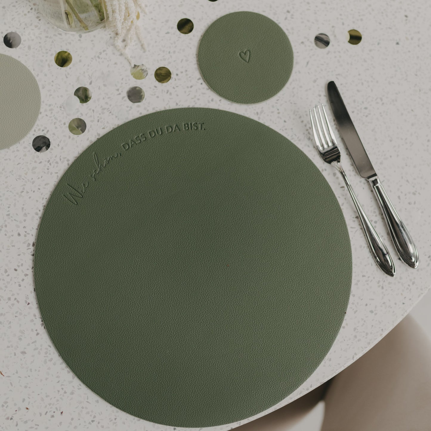 Grünes Platzset mit eingeprägtem Spruch ‚Wie schön, dass du da bist‘ neben Besteck auf gedecktem Tisch