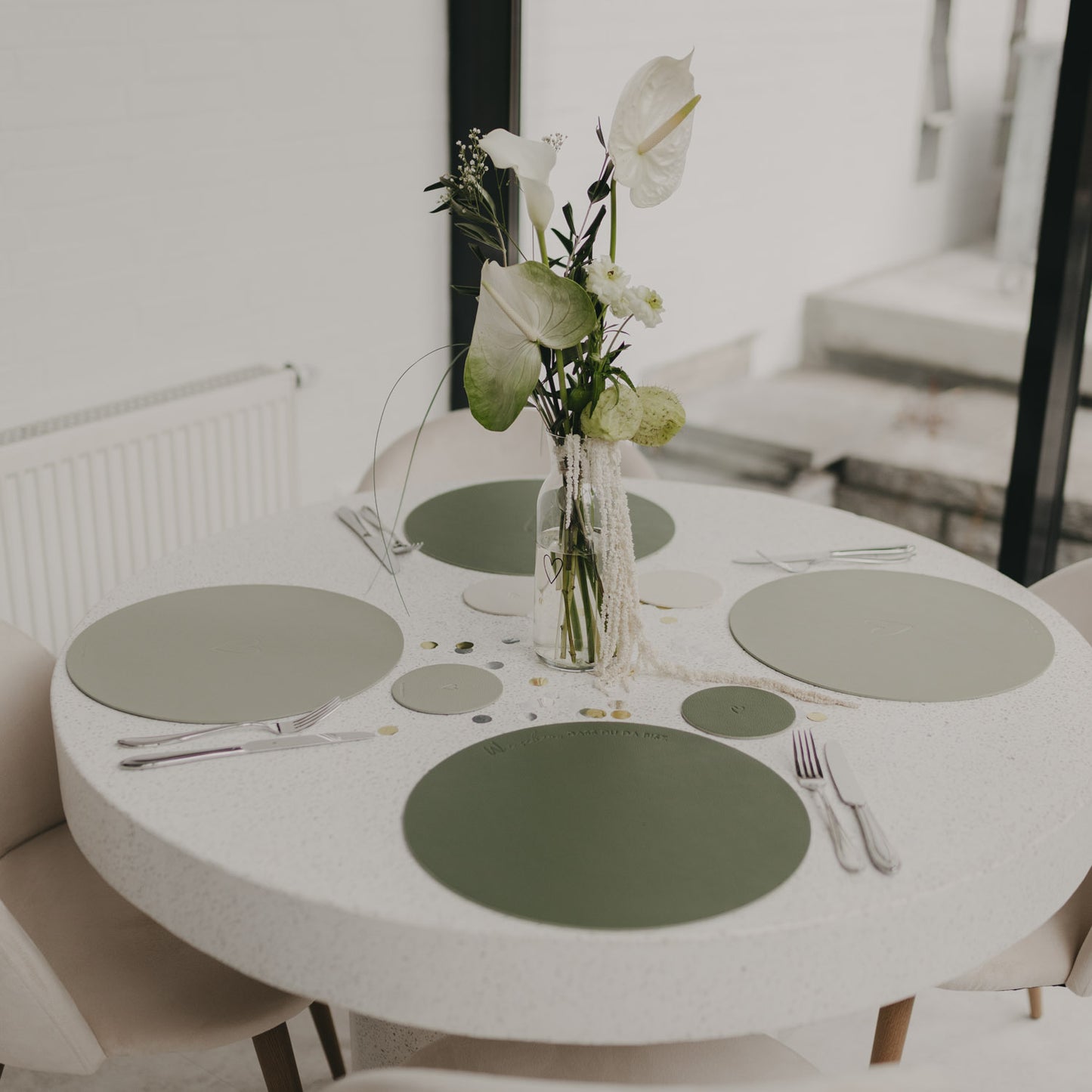 Rund gedeckter Tisch mit grünen wendbaren Platzsets und Blumendekoration.