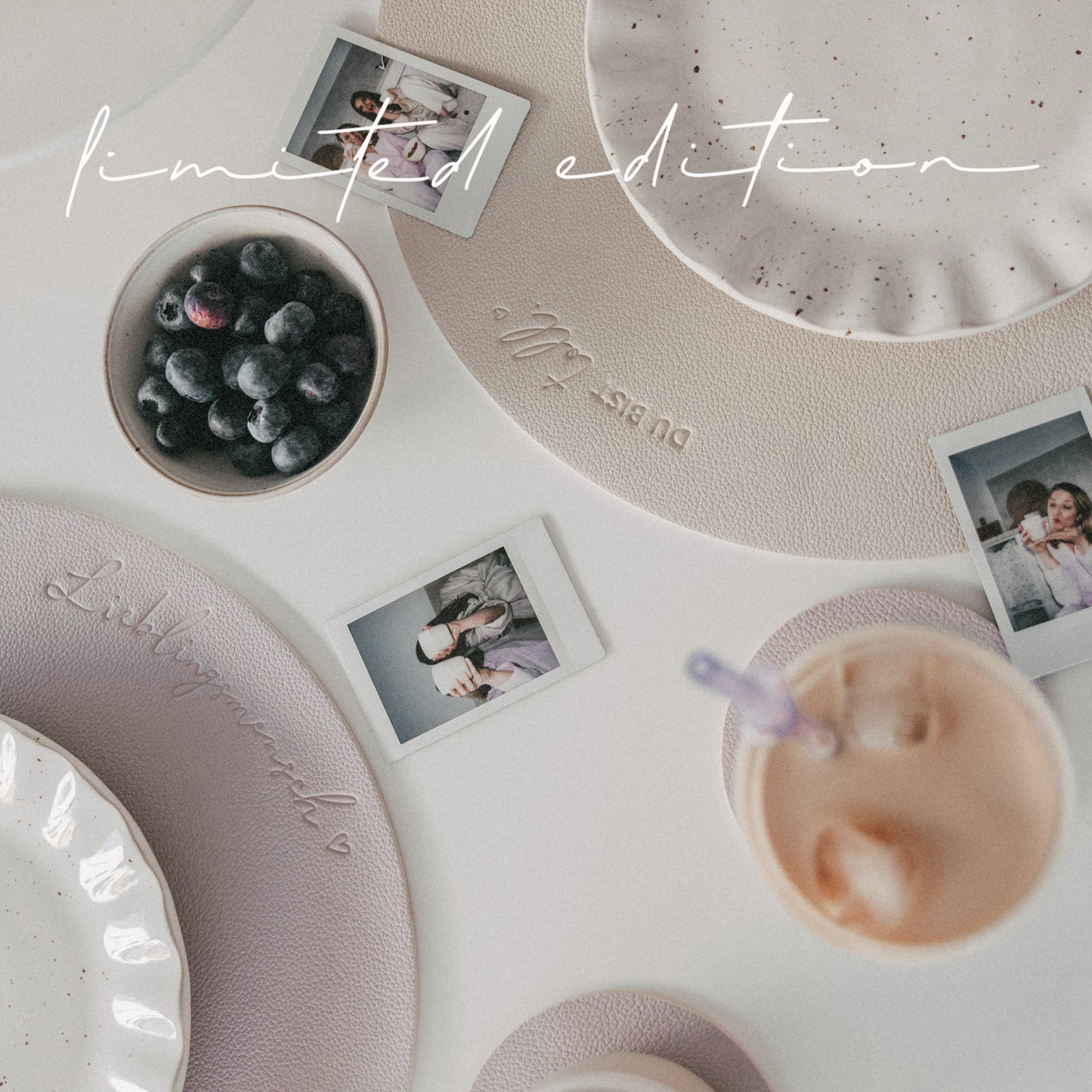 Gedeckter Tisch mit fliederfarbenem Platzset „Lieblingsmensch“, Geschirr, Beeren und Fotos.