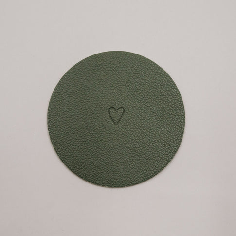 Runder grüner Untersetzer mit geprägtem Herzmotiv auf hellem Hintergrund.