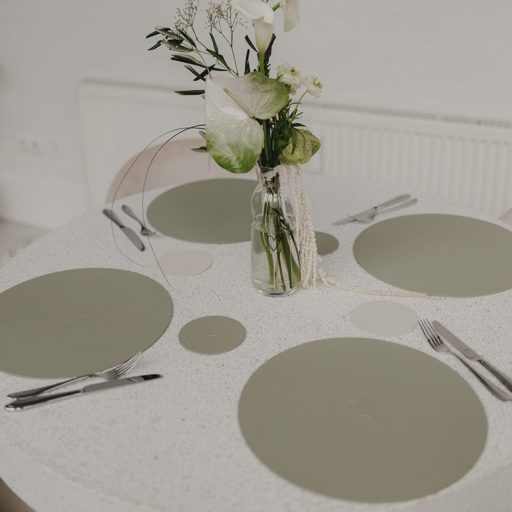 Gedeckter Tisch mit grünen Platzsets und passenden Untersetzern in Grün.