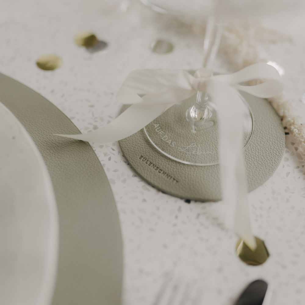 Detailaufnahme: Hellgrüner Untersetzer mit Sektglas und dekorativer Schleife.