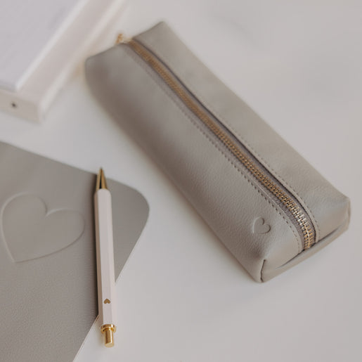 Graue Federtasche mit Herzprägung und goldenem Reißverschluss von Eulenschnitt neben Notizbuch und Stift