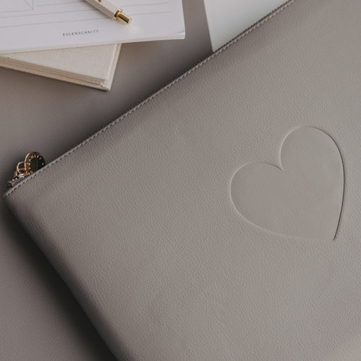 Graues Laptop Sleeve mit Herzprägung von Eulenschnitt auf Schreibtisch mit Notizblock und Stift