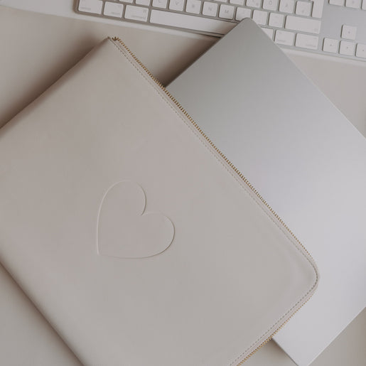Cremefarbene Laptophülle mit Herzprägung und Reißverschluss, auf Schreibtisch neben Laptop und Tastatur