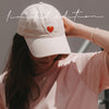 Frau mit beiger Cap mit roter Herz-Stickerei und rosa T-Shirt