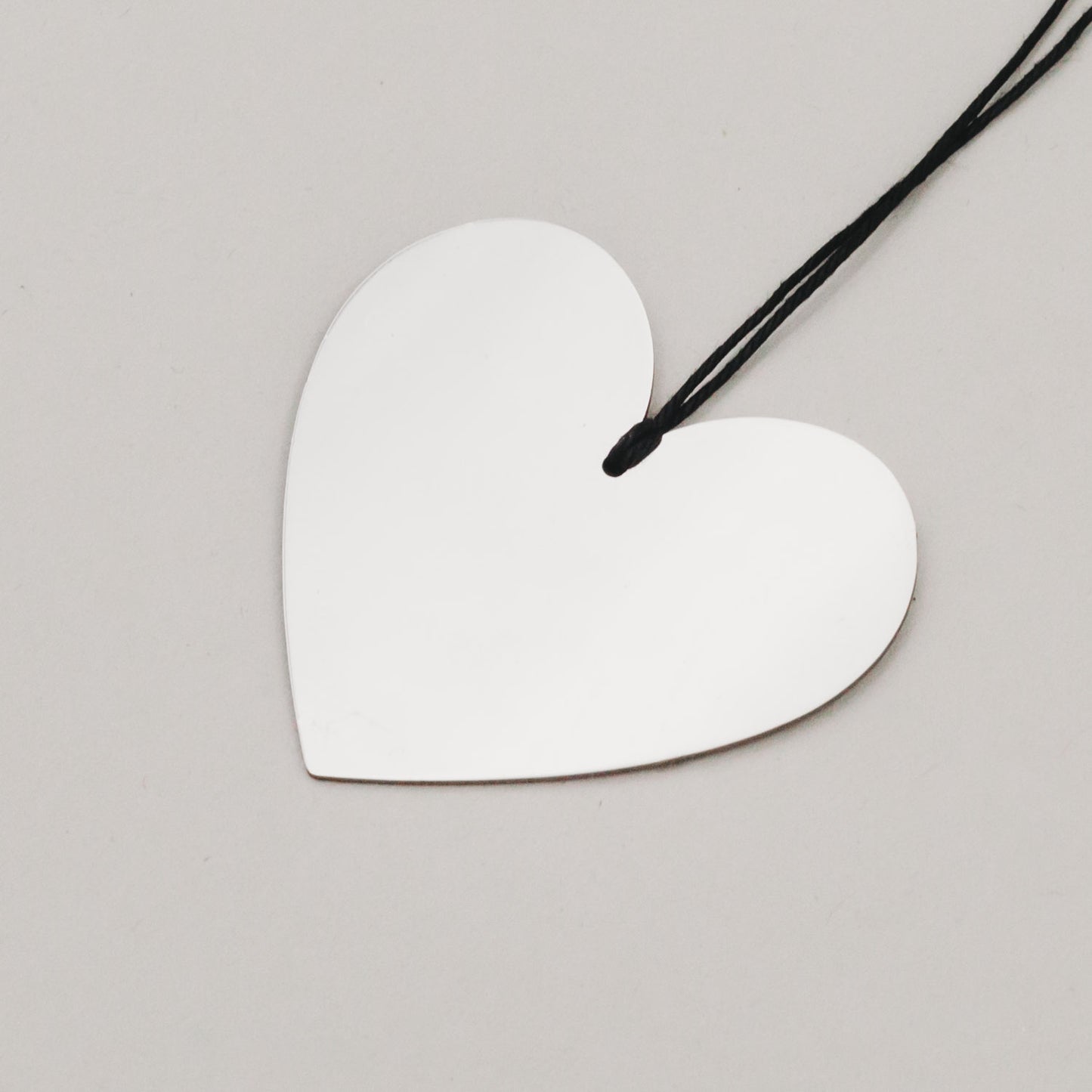 Detailaufnahme eines silbernen Herzanhängers aus Metall mit schwarzer Aufhängung