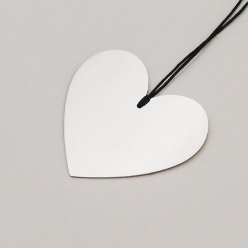 Detailaufnahme eines silbernen Herzanhängers aus Metall mit schwarzer Aufhängung