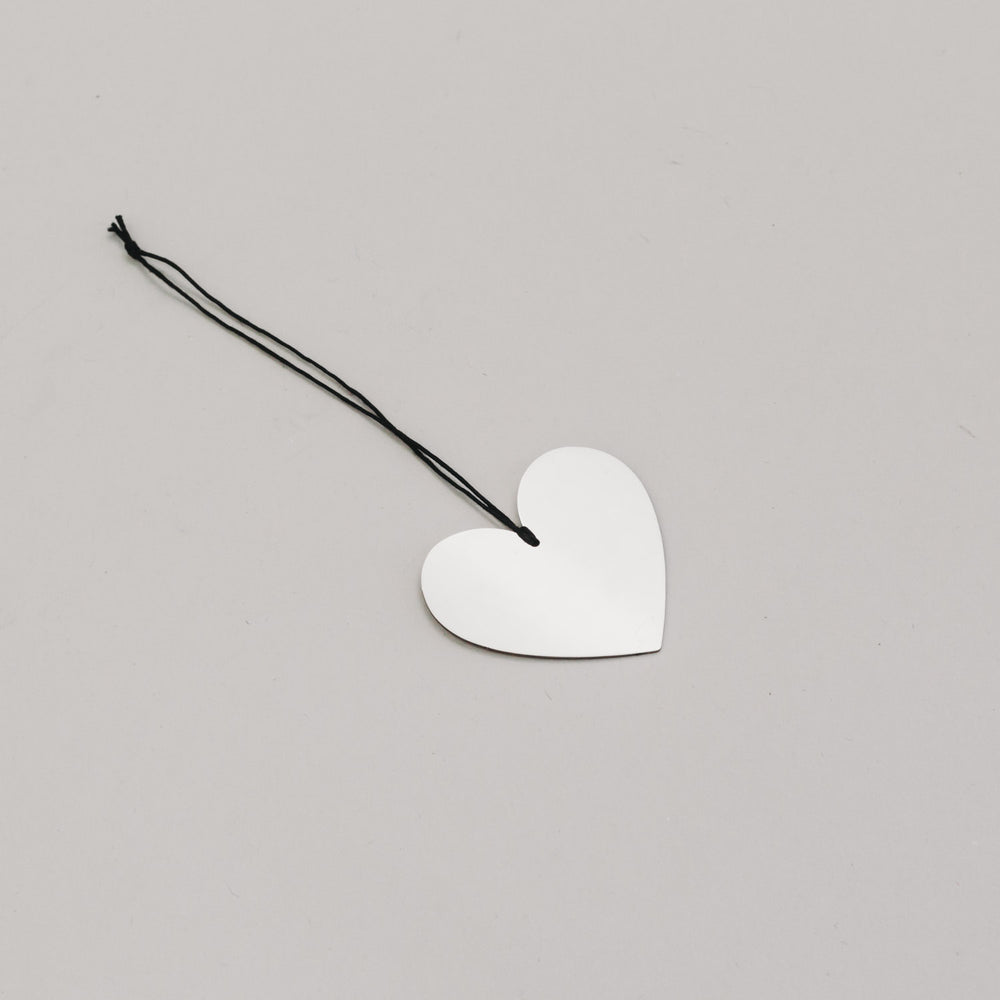 Silbernes Herz aus Metall mit schwarzem Band – flach auf hellem Untergrund fotografiert