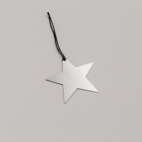 Schlichter silberner Sternanhänger aus Metall mit schwarzem Band, auf hellem Untergrund liegend.