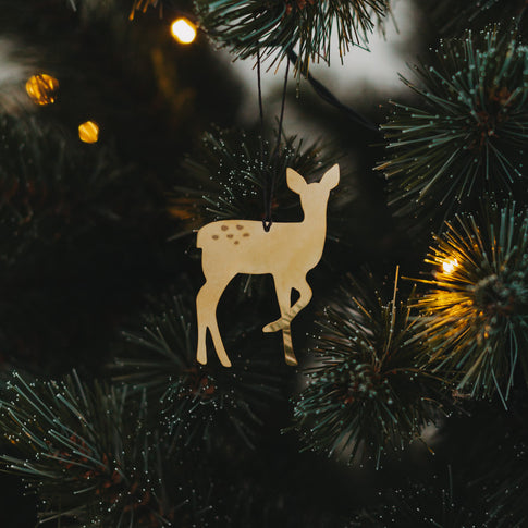 Glänzender goldener Rehanhänger am Weihnachtsbaum mit feinen Lichterketten im Hintergrund.
